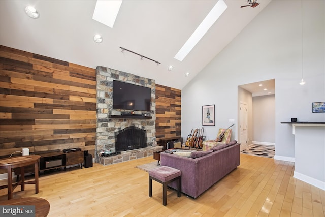 living room featuring a skylight, a fireplace, light hardwood / wood-style floors, and high vaulted ceiling