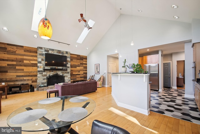 living room featuring light hardwood / wood-style floors, high vaulted ceiling, a stone fireplace, a skylight, and wooden walls