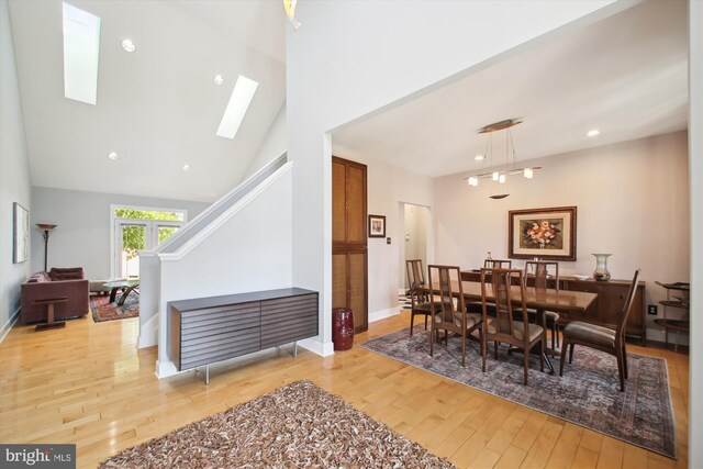 dining room with a skylight, light hardwood / wood-style floors, and high vaulted ceiling