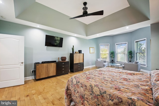 bedroom with ceiling fan, a raised ceiling, and light hardwood / wood-style floors