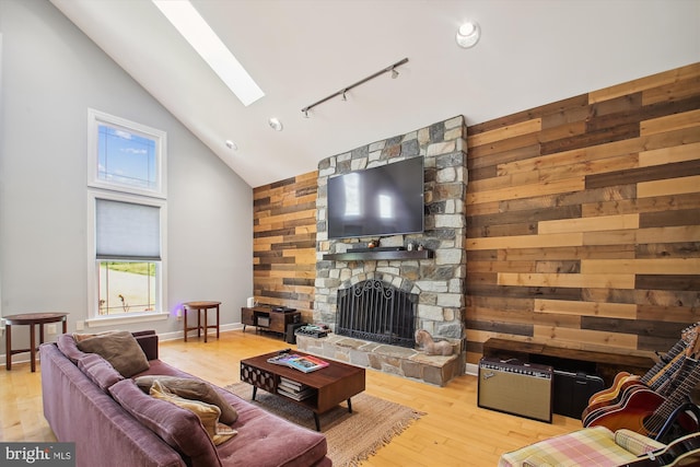 living room featuring light hardwood / wood-style floors, rail lighting, high vaulted ceiling, a skylight, and a stone fireplace