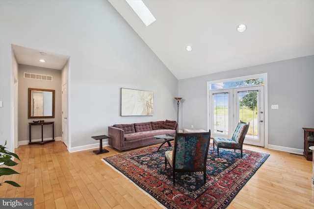 living room featuring light hardwood / wood-style floors, a skylight, and high vaulted ceiling