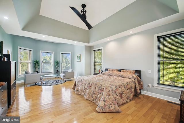 bedroom featuring ceiling fan, light wood-type flooring, a tray ceiling, and multiple windows