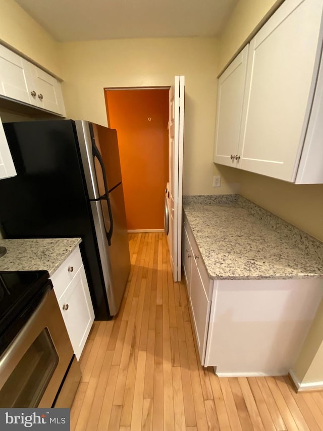 kitchen with appliances with stainless steel finishes, light stone counters, light hardwood / wood-style flooring, and white cabinets