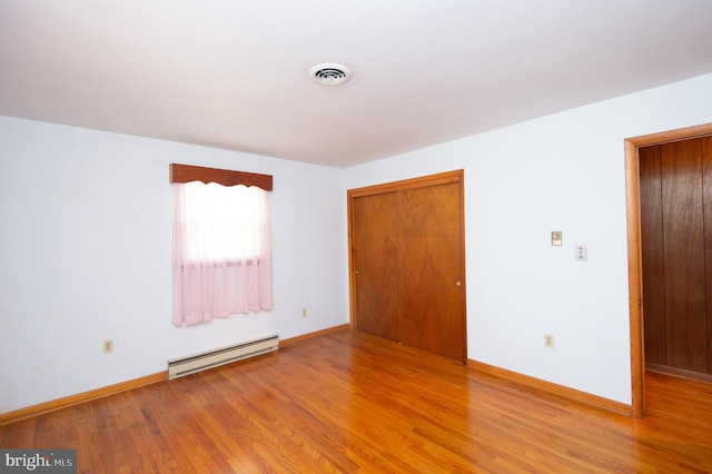 unfurnished bedroom with a baseboard heating unit, hardwood / wood-style flooring, and a closet