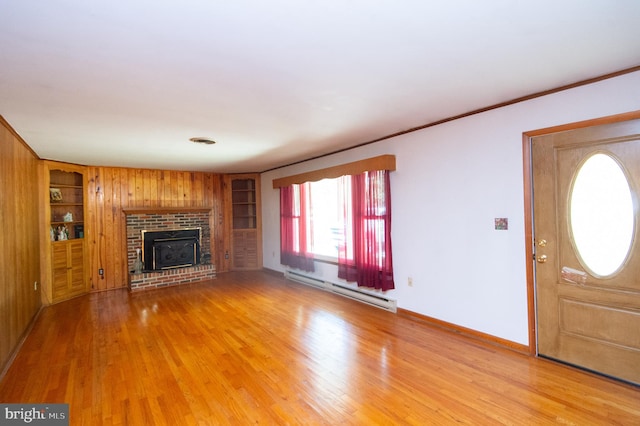 unfurnished living room with wooden walls, built in features, a brick fireplace, wood-type flooring, and a baseboard heating unit