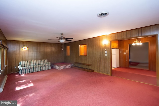 interior space featuring white refrigerator, ceiling fan with notable chandelier, and wooden walls