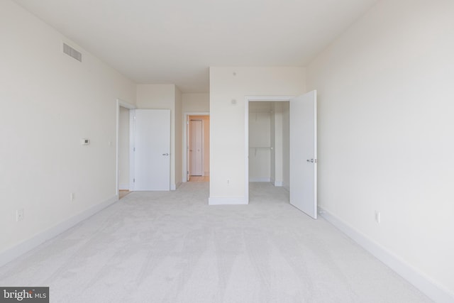 unfurnished bedroom featuring visible vents, a walk in closet, baseboards, light carpet, and a closet