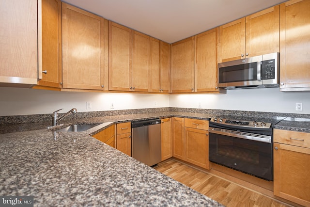 kitchen with dark stone countertops, sink, stainless steel appliances, and light hardwood / wood-style flooring