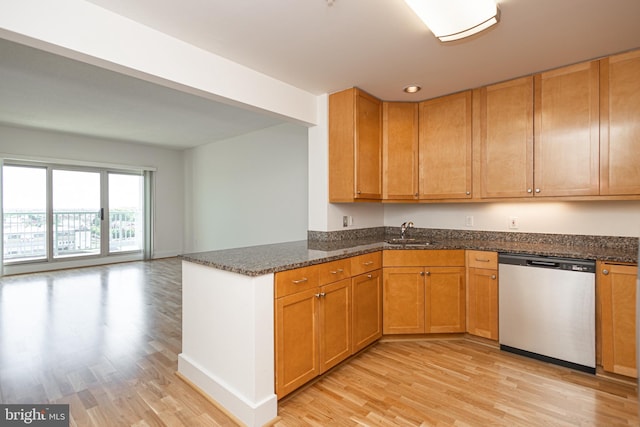 kitchen with a sink, dishwasher, dark stone countertops, and light wood finished floors