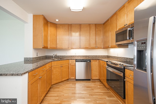 kitchen featuring sink, stainless steel appliances, light hardwood / wood-style flooring, kitchen peninsula, and dark stone counters