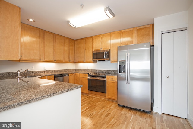 kitchen featuring sink, kitchen peninsula, dark stone countertops, light hardwood / wood-style floors, and appliances with stainless steel finishes