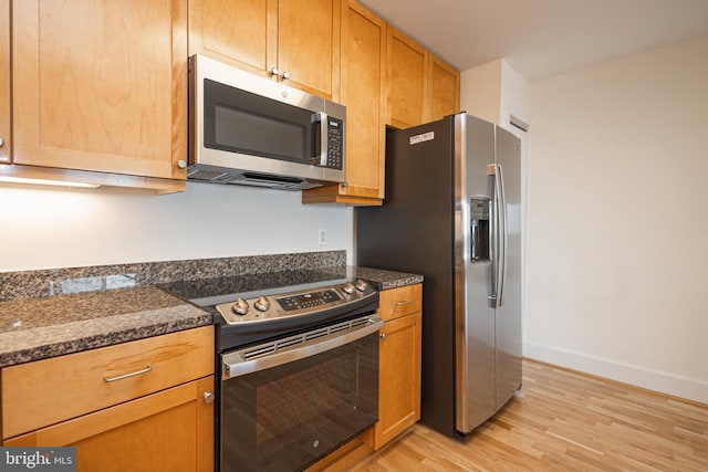 kitchen with dark stone countertops, light wood-style flooring, baseboards, and appliances with stainless steel finishes