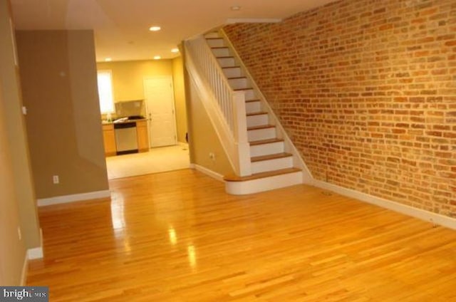 unfurnished living room with light hardwood / wood-style flooring and brick wall