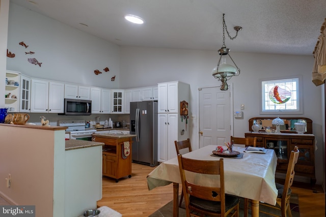 dining room with light hardwood / wood-style flooring, a textured ceiling, and high vaulted ceiling