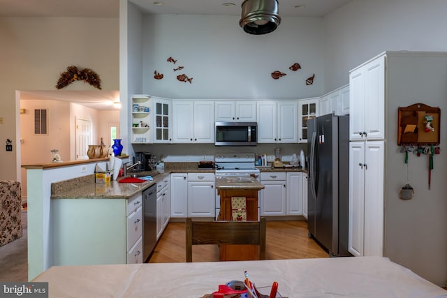 kitchen with white cabinets, stainless steel appliances, a high ceiling, and light stone countertops