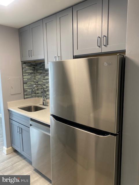 kitchen with light hardwood / wood-style flooring, stainless steel appliances, backsplash, and sink