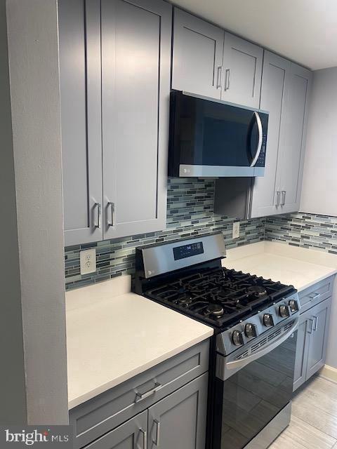 kitchen featuring light wood-type flooring, gray cabinets, appliances with stainless steel finishes, and backsplash