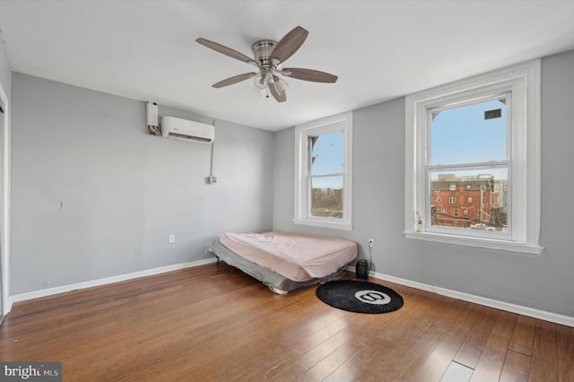 unfurnished bedroom featuring a wall mounted air conditioner, wood-type flooring, and ceiling fan