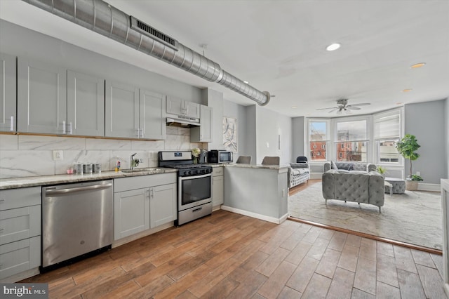 kitchen with wood-type flooring, appliances with stainless steel finishes, ceiling fan, and decorative backsplash