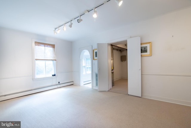 empty room with light carpet, baseboard heating, and rail lighting