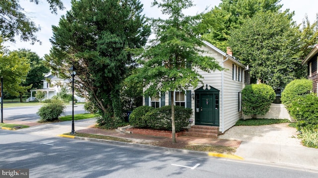 view of property hidden behind natural elements with entry steps, a chimney, and fence