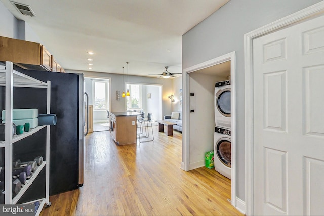 kitchen featuring stacked washing maching and dryer, light hardwood / wood-style flooring, ceiling fan, and a breakfast bar area