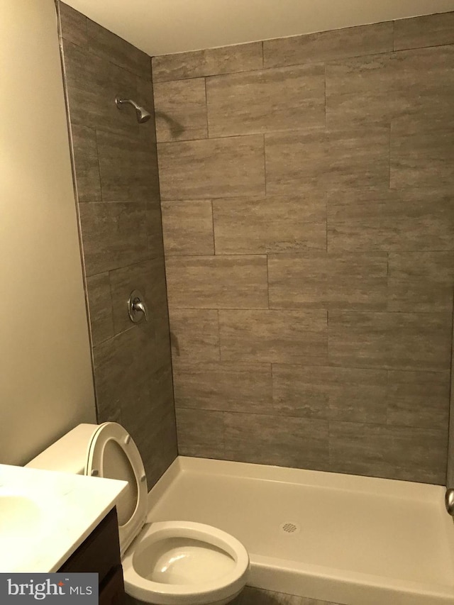 full bathroom with a tile shower, toilet, and vanity