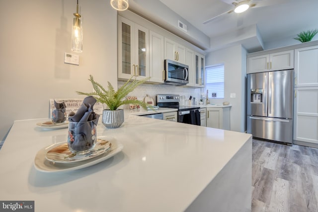 kitchen with appliances with stainless steel finishes, light wood-type flooring, white cabinetry, and decorative backsplash