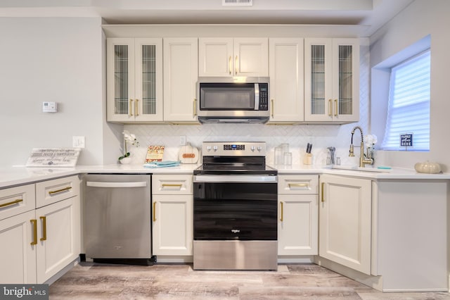 kitchen featuring sink, tasteful backsplash, light hardwood / wood-style flooring, white cabinetry, and stainless steel appliances