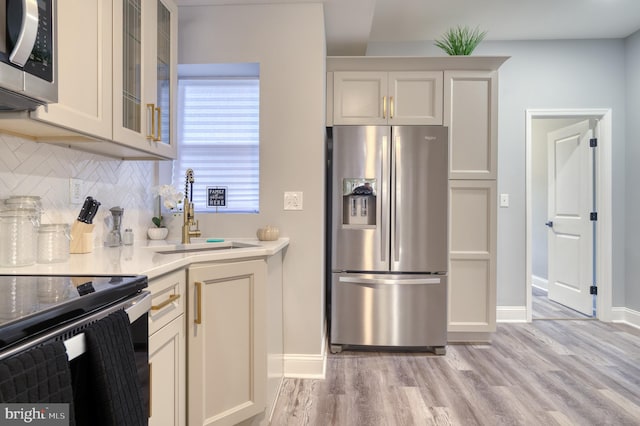 kitchen featuring decorative backsplash, stainless steel appliances, light wood-type flooring, and sink