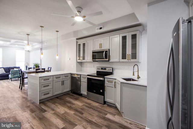 kitchen featuring dark wood-type flooring, sink, kitchen peninsula, stainless steel appliances, and decorative light fixtures