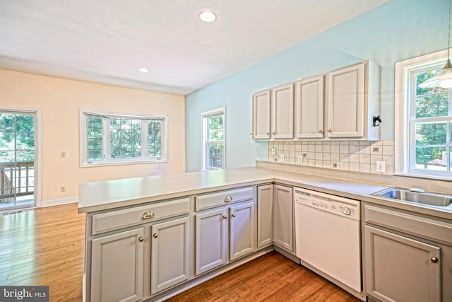 kitchen featuring tasteful backsplash, decorative light fixtures, dishwasher, kitchen peninsula, and light hardwood / wood-style floors