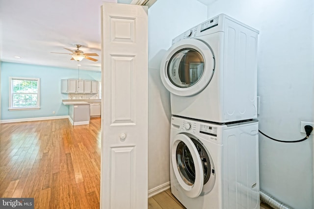 clothes washing area featuring stacked washing maching and dryer, ceiling fan, and light wood-type flooring