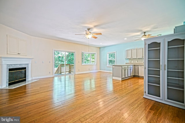 unfurnished living room with a fireplace, a wealth of natural light, ceiling fan, and light hardwood / wood-style floors