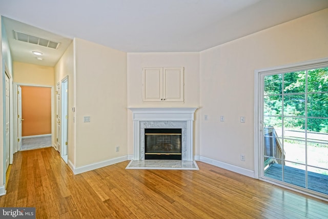 unfurnished living room with light wood-type flooring, a high end fireplace, and a healthy amount of sunlight