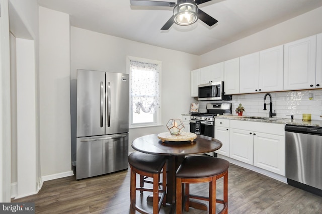 kitchen with light stone countertops, dark hardwood / wood-style flooring, stainless steel appliances, ceiling fan, and sink