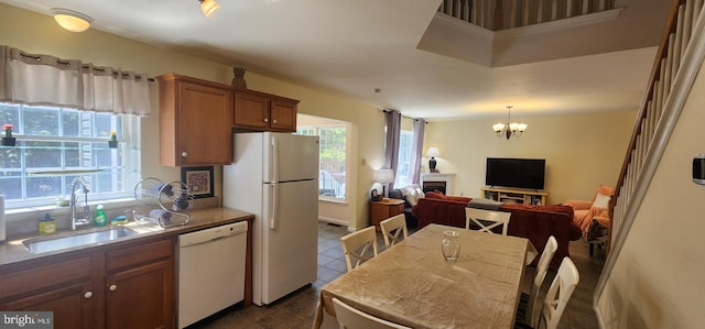 kitchen featuring dark tile patterned flooring, decorative light fixtures, white appliances, a notable chandelier, and sink