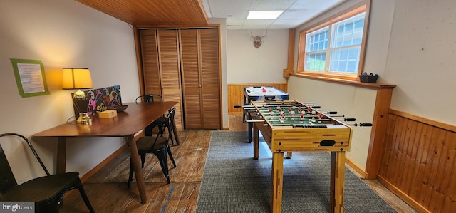 game room with hardwood / wood-style floors, wooden walls, and a drop ceiling