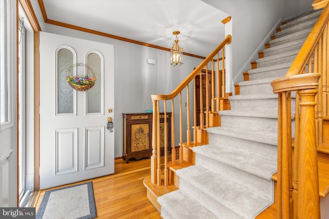 foyer entrance with an inviting chandelier, crown molding, and light hardwood / wood-style floors