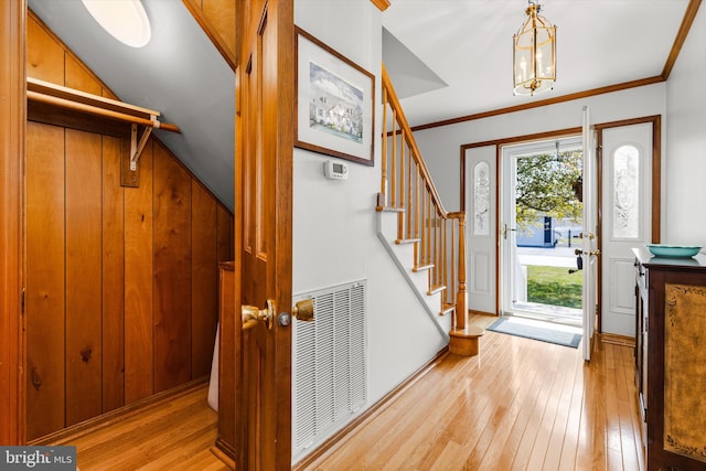 entryway featuring crown molding, wood walls, an inviting chandelier, and light hardwood / wood-style flooring