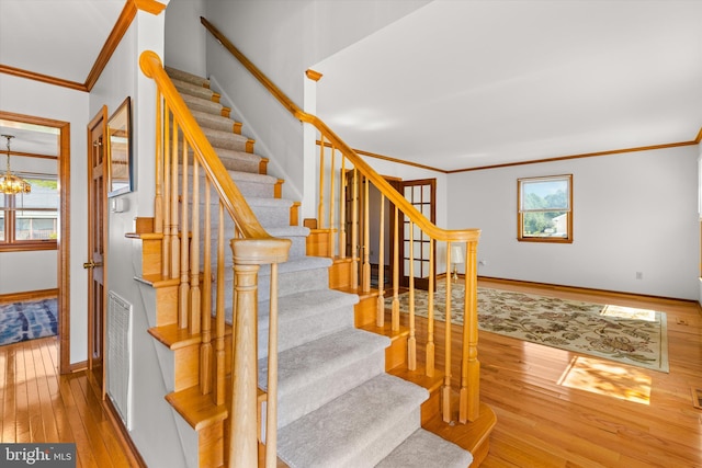 stairs with wood-type flooring, plenty of natural light, crown molding, and a notable chandelier