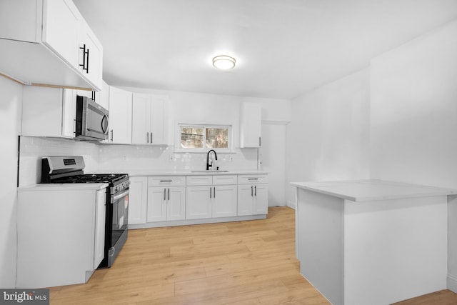 kitchen with light wood-type flooring, sink, stainless steel appliances, and white cabinets