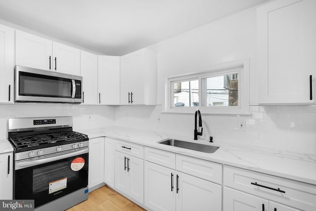 kitchen with light stone countertops, light hardwood / wood-style flooring, stainless steel appliances, sink, and white cabinetry