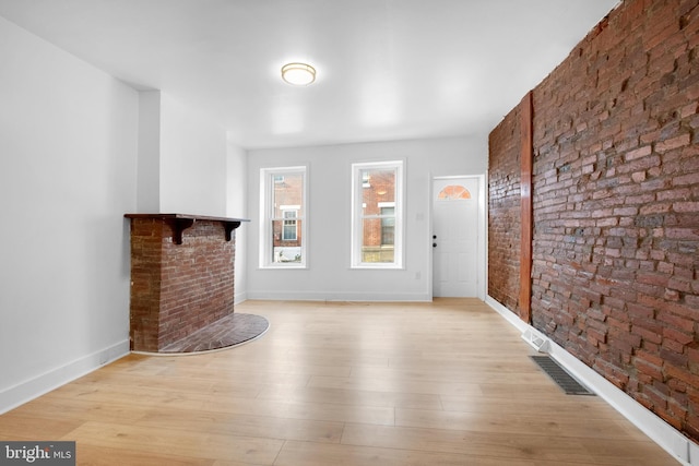 unfurnished living room with light wood-style floors, visible vents, brick wall, and baseboards