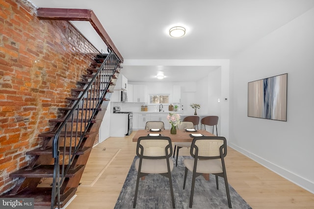 dining area featuring light wood finished floors, brick wall, stairs, and baseboards