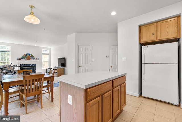 kitchen featuring a fireplace, decorative light fixtures, light tile patterned floors, a kitchen island, and white refrigerator