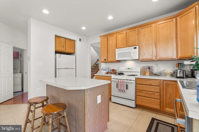 kitchen with white appliances, a center island, a breakfast bar, washer / dryer, and light tile patterned flooring