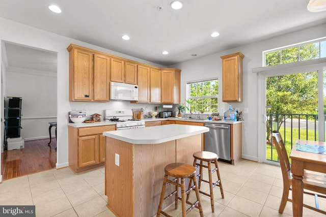 kitchen with white appliances, a kitchen bar, a center island, and light tile patterned flooring