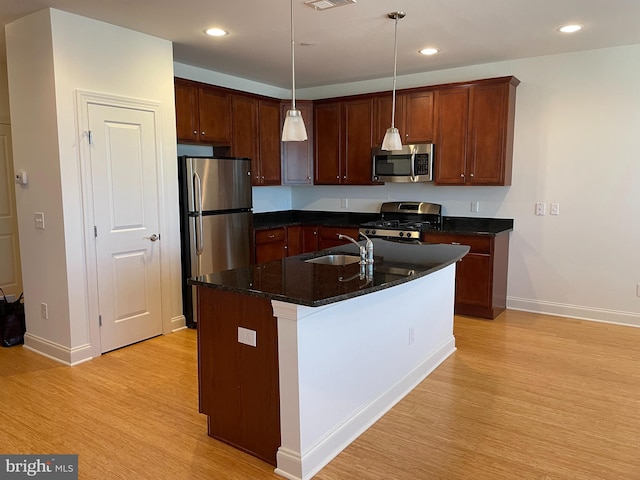 kitchen featuring sink, an island with sink, hanging light fixtures, light hardwood / wood-style flooring, and appliances with stainless steel finishes